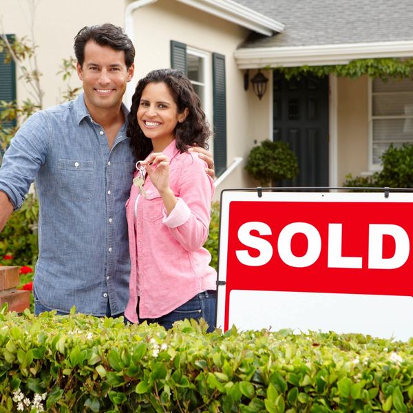 Happy couple holding keys in front of their newly sold house.
