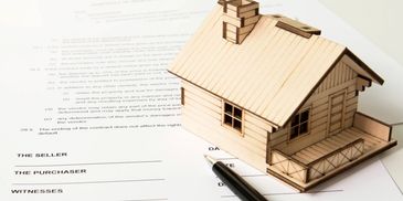 A wooden house model on a real estate contract with a pen.