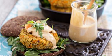 Vegan chickpea burger with creamy sauce and arugula on dark bread.