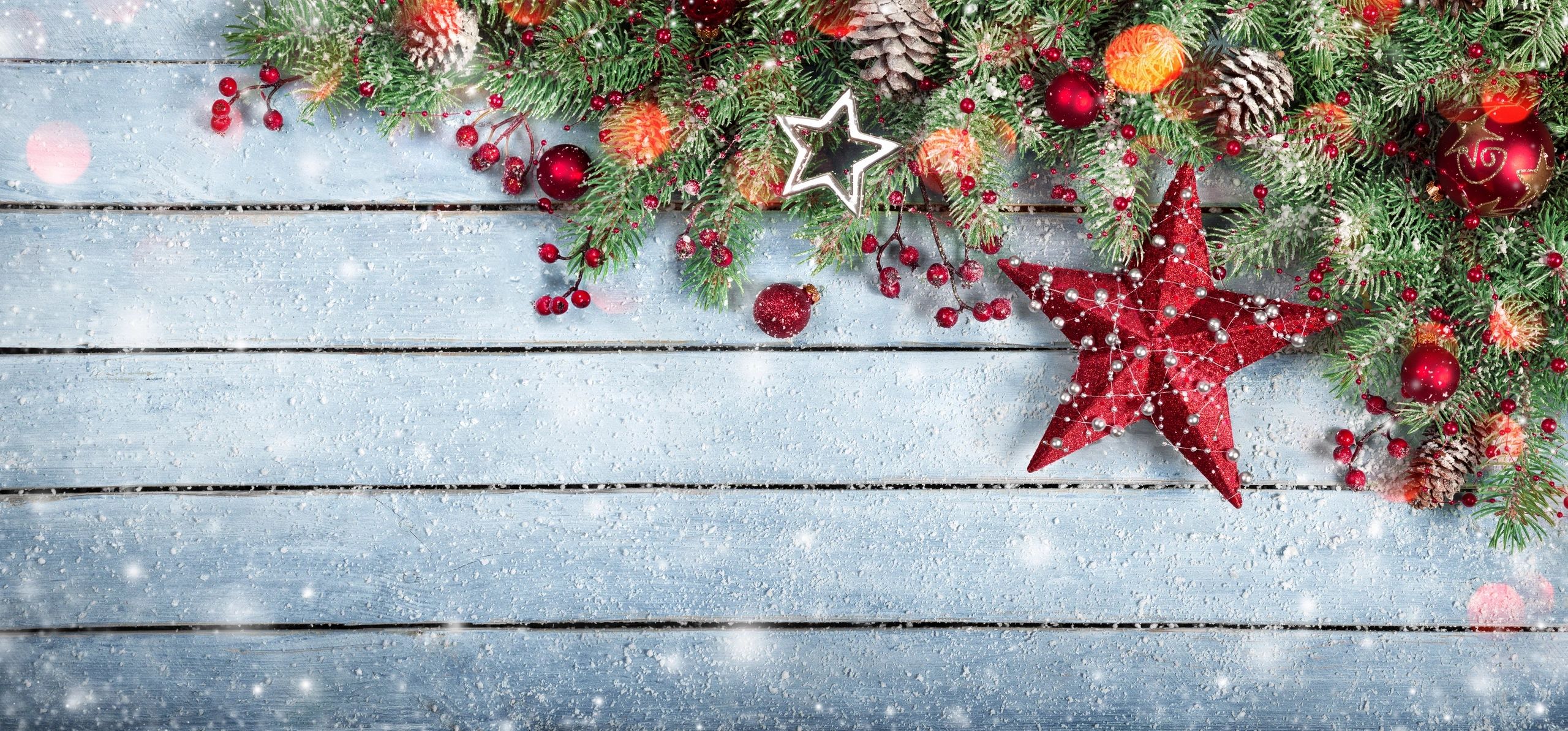 Festive Christmas decorations with pinecones, red berries, and ornaments on a snowy wooden background.