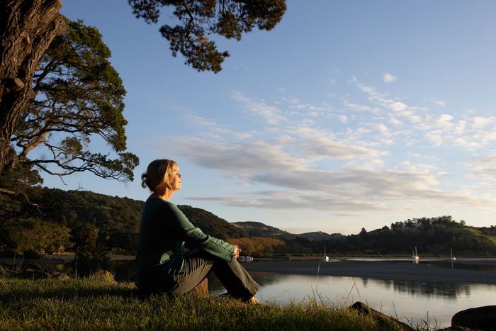 Woman sitting peacefully by a lake at sunset, enjoying nature's tranquility.