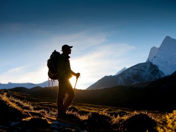 Hiker silhouetted against a mountain backdrop at sunrise.
