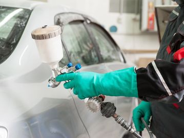 Men performing an auto body painting of a white car.