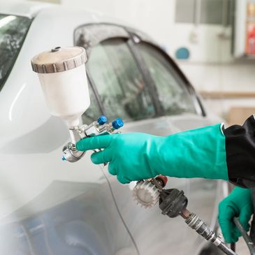A technician in green gloves uses a spray gun to paint a car