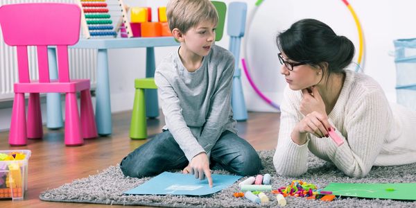 A female speech language pathologist teaching a male child on a fluffy grey rug