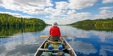 Person paddling in a canoe on a calm lake.