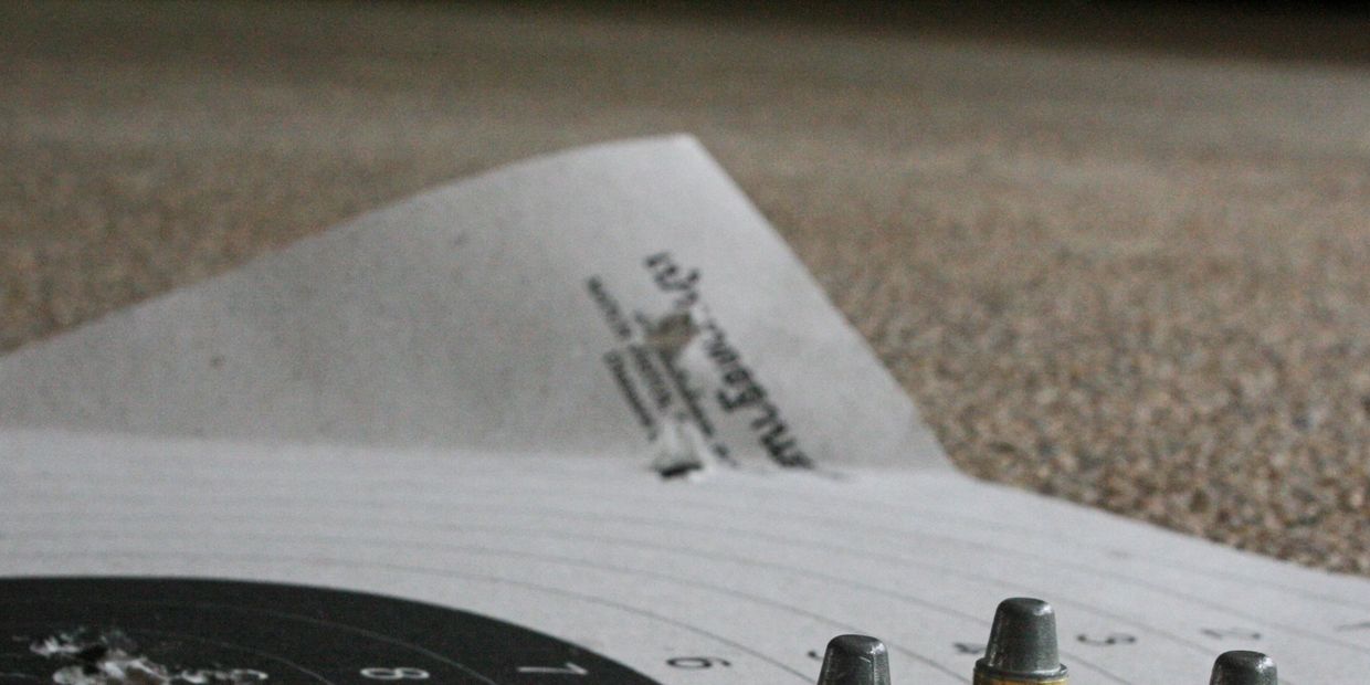 Bullets placed on a shooting target paper on a carpeted surface.