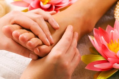 Hands giving a foot massage near pink flowers for relaxation.