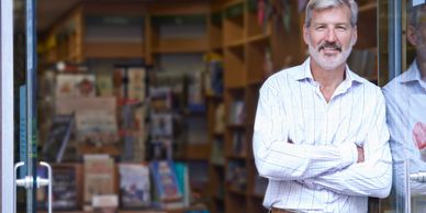 small business owner in front of his bookshop - older man with arms folded smiling at camera