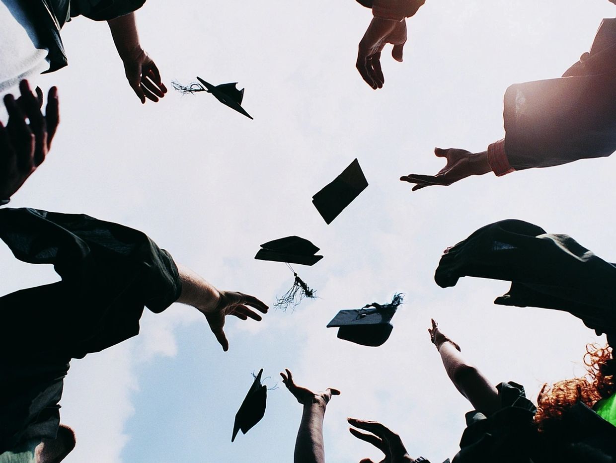 Graduates celebrate by tossing caps into the sky against a bright sky.