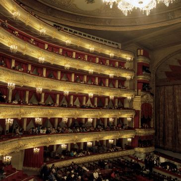 Elegant multi-tiered theater interior with chandeliers and audience.