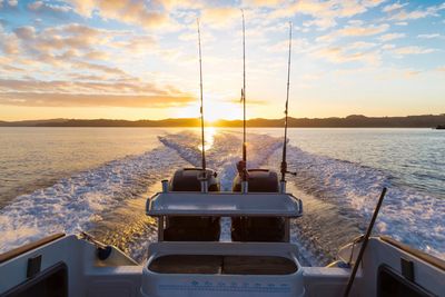 Fishing rods on a boat at sunset over calm water.