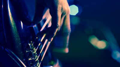 Close-up of a hand playing a guitar under dim blue lighting.