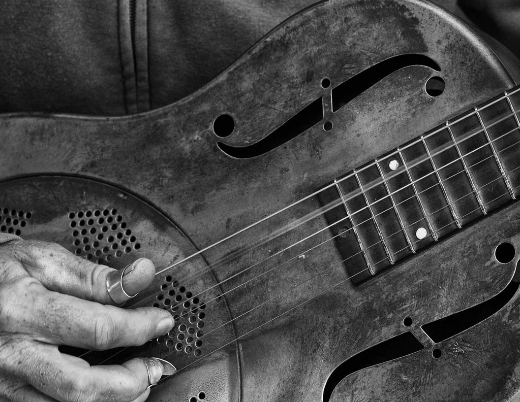 Close-up of a hand playing a vintage steel resonator guitar in black and white.