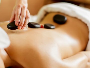 Person receiving a hot stone massage with smooth black stones on their back.
