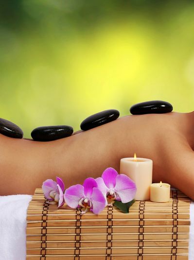 Woman receiving hot stone massage with flowers and candles.