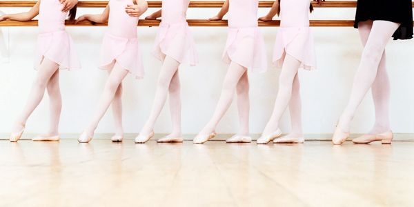 Young ballet dancers practicing at the barre in pink tutus and tights.