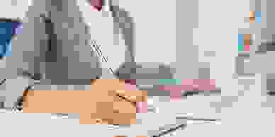 Businesswoman writing in a diary sitting at an office desk.