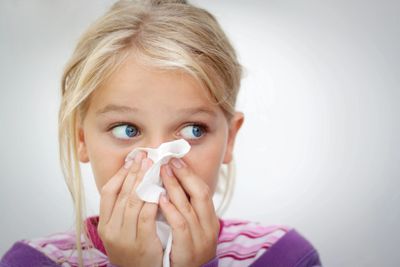 little girl sick with cold and flu blowing nose with tissue