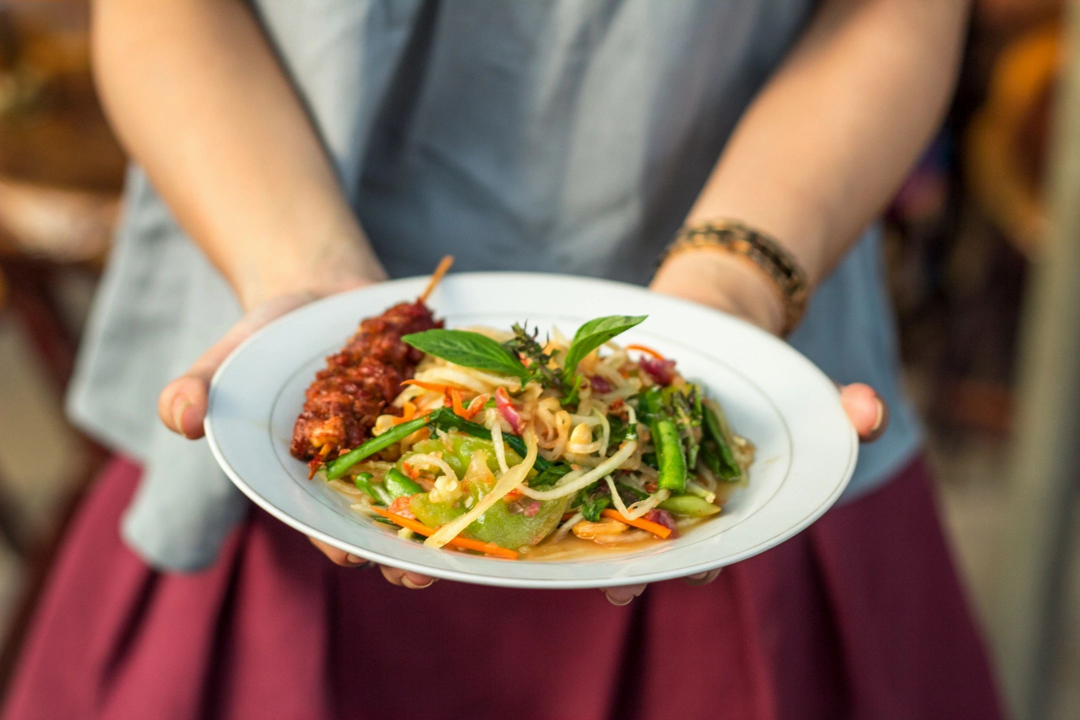 Person holding a plate of colorful vegetable stir-fry with a skewer.