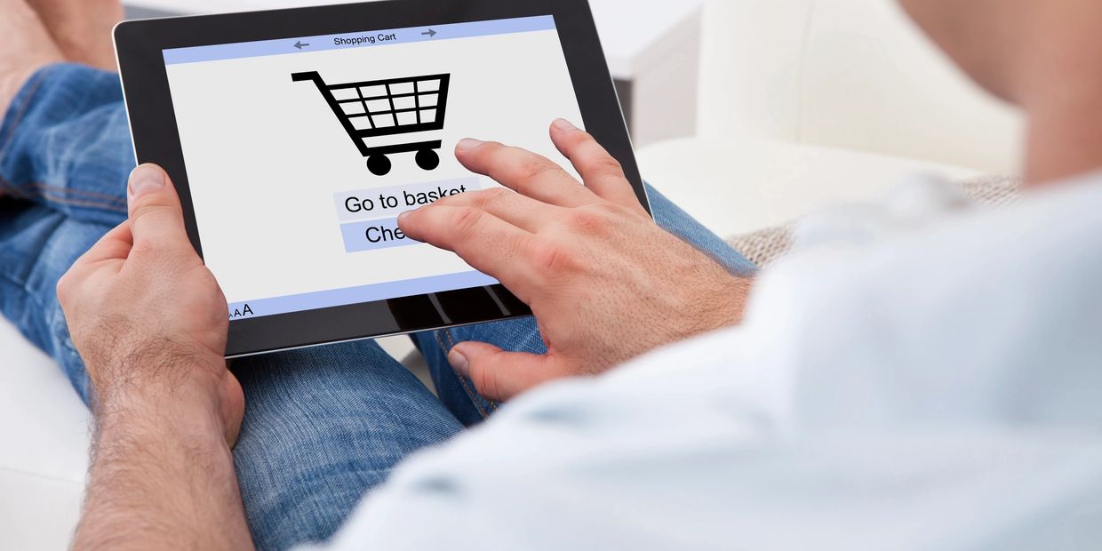 Person shopping online using a tablet with a shopping cart icon.