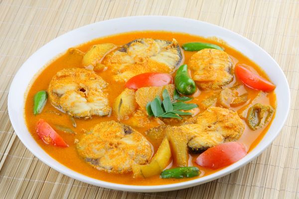 A bowl of fish curry with green chilies and tomatoes.