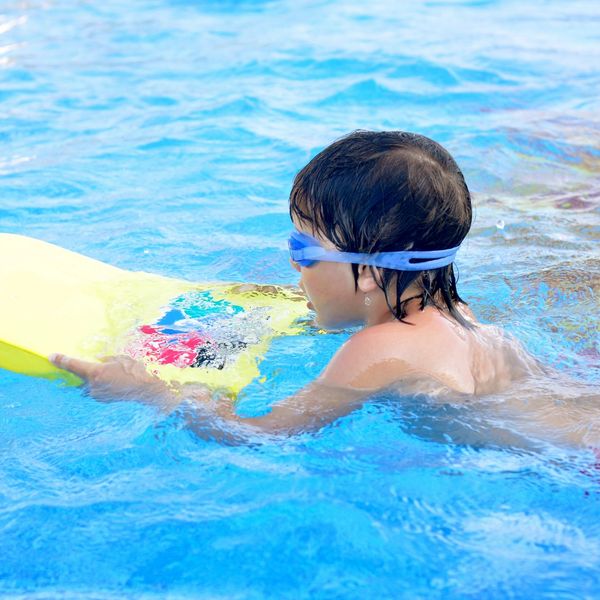 Young child swimming in pool with yellow foam kick board.