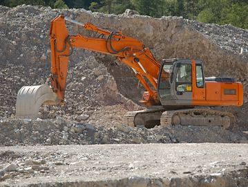 Orange excavator parked on rocky terrain at a construction site.