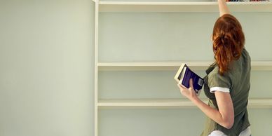 someone putting books onto clean white bookshelves