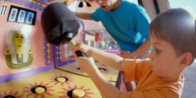 Young boy playing a hammer game at an arcade.