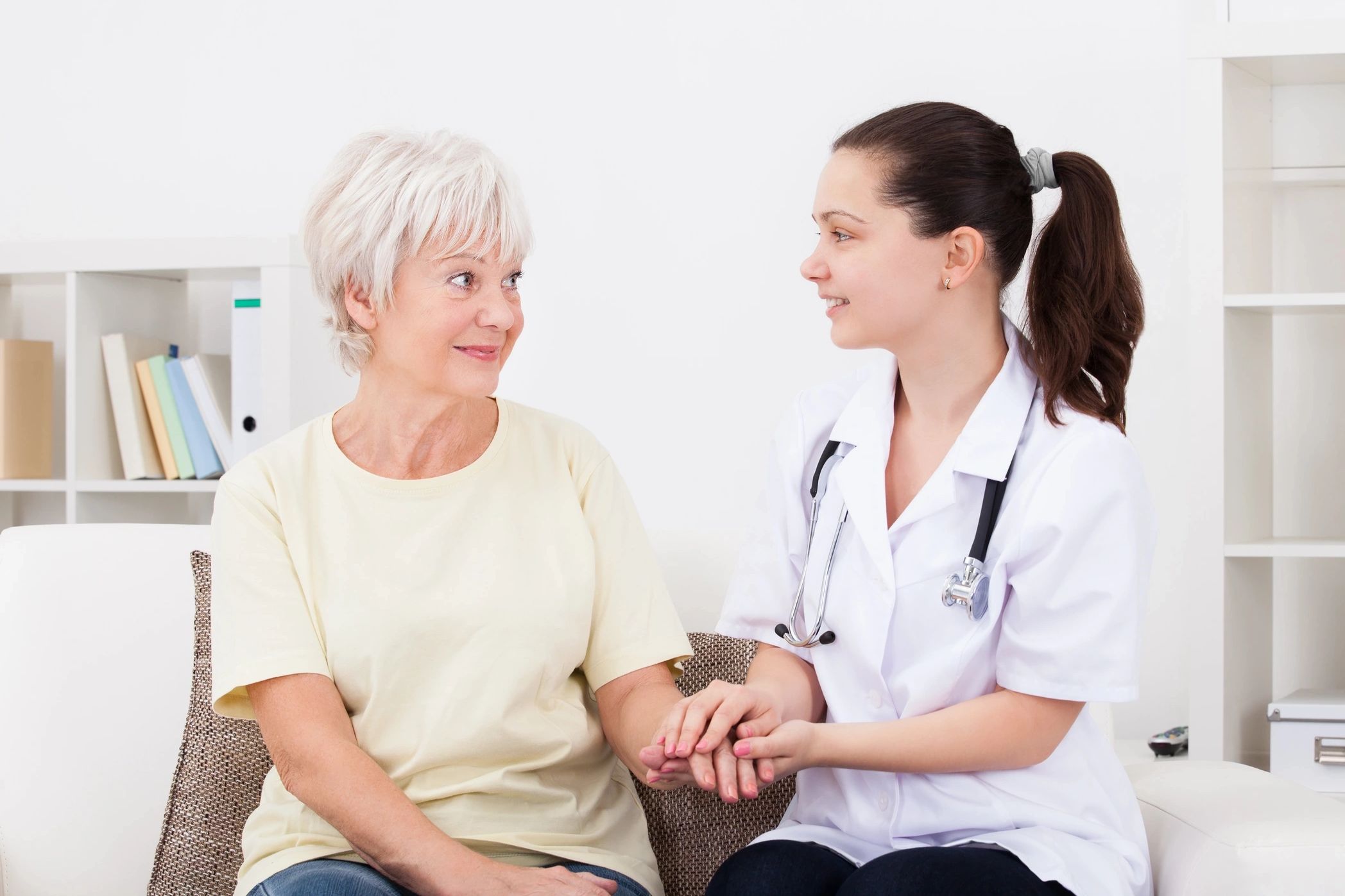 A nurse warmly holding an elderly patient's hand during a home visit. 