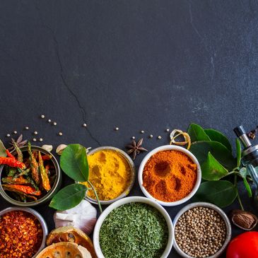 Colorful spices and fresh herbs arranged on a dark surface.