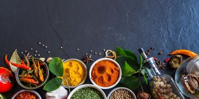 Colorful spices and herbs arranged on a dark stone surface.