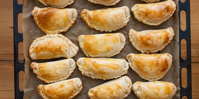 Tray of golden-brown baked empanadas on parchment paper.
