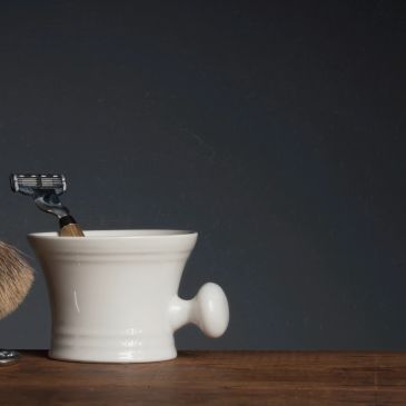 Classic shaving set with brush and razor beside a white ceramic bowl.