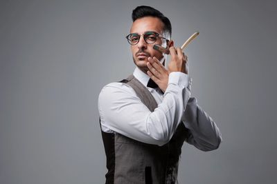 A man with glasses and a vest applies shaving cream with a brush.