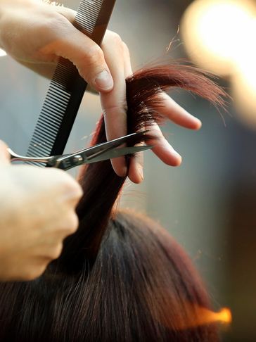 A close-up of a hairdresser cutting hair with scissors and a comb.