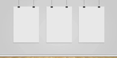 Three blank white posters hanging on a gray wall above a wooden floor.
