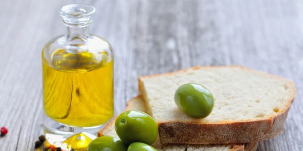Green olives, olive oil bottle, and slices of bread on a rustic table.