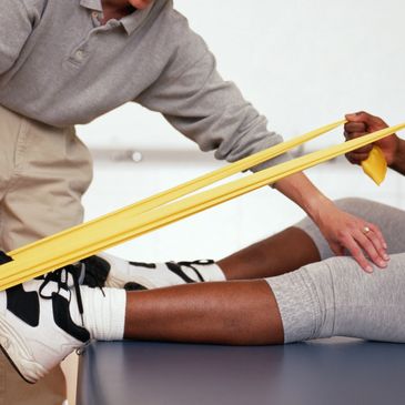 A woman stretching her legs on a table with the help of a person