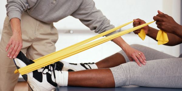 physiotherapist helping a patient exercise their left ankle with a yellow elastic band