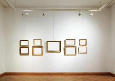 Empty picture frames of various sizes arranged on a white gallery wall.