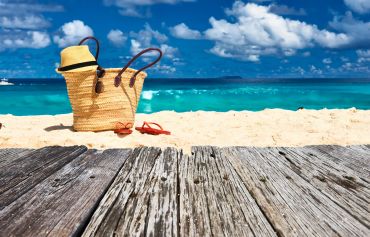 Beach scene with tote bag, sunglasses, and hat on sand.
