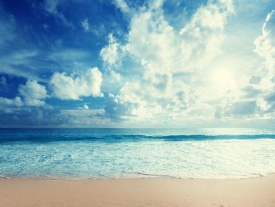 Bright sun shines over a calm ocean with gentle waves at the sandy beach.