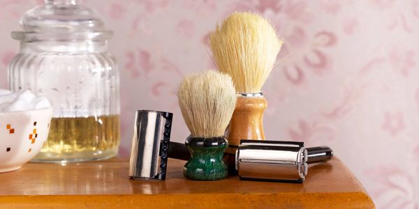 Vintage shaving brushes and razors on a wooden surface with a glass jar and bowl.