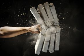 A fist breaking through a concrete block with dust flying.