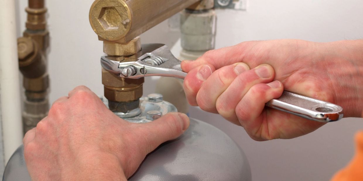Hands using a wrench to tighten a valve on a gas cylinder.