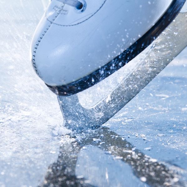 Close-up of an ice skate blade cutting into ice, spraying ice particles.
