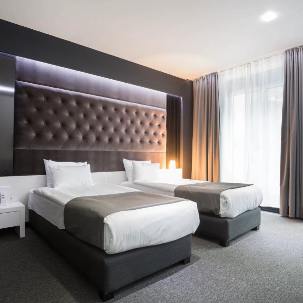 Modern hotel room with two single beds and soft lighting.