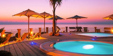 Sunset view of a poolside with beach umbrellas and sea.